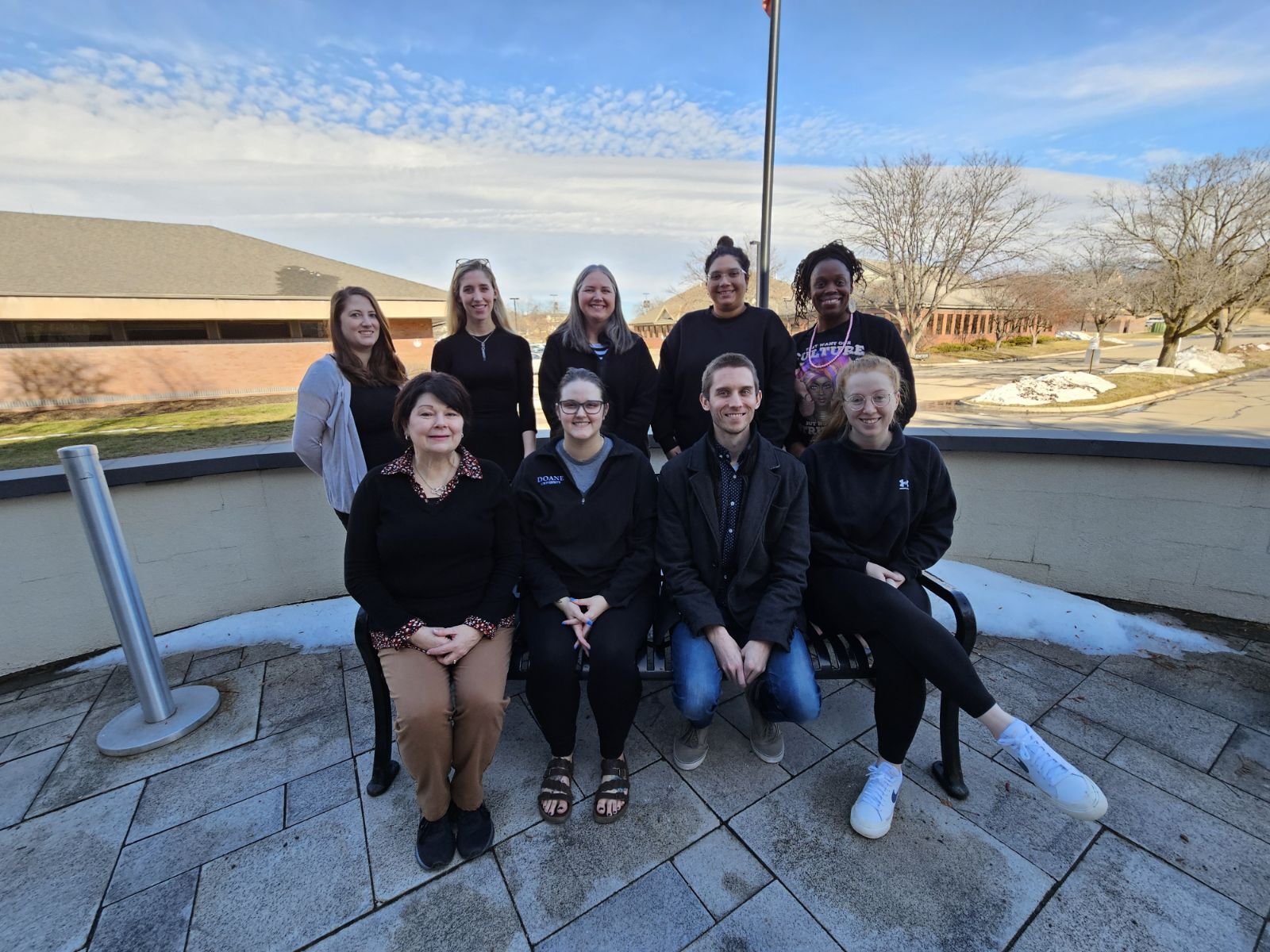 Doane employees from the Academic Success Center, Academic Affairs and the Registrar's office pose in two rows on a bench outside of the Fred Brown Center.