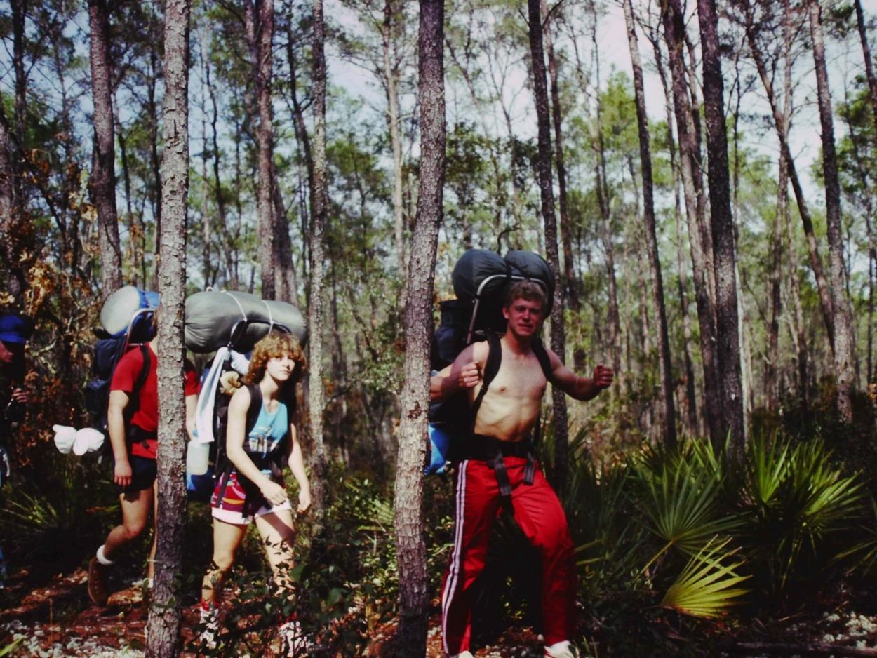 Students carrying large packs hike through a forest in the southeast United States.