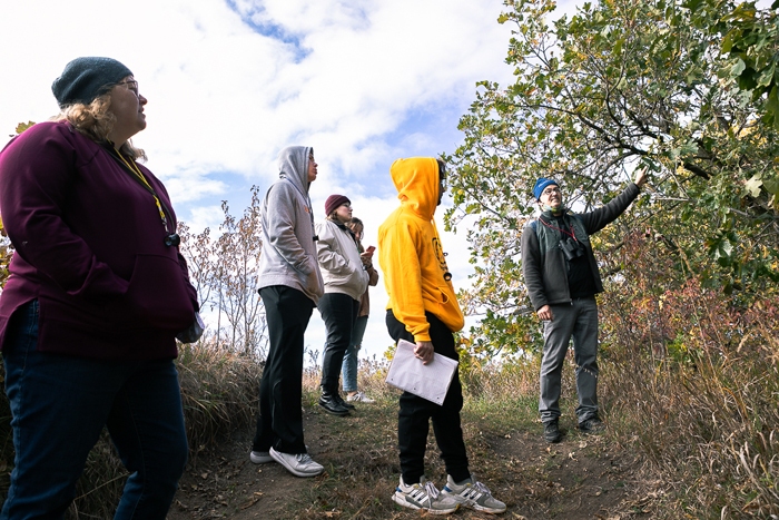 Jason St. Saveur (far right), senior education manager for Spring Creek Prairie Audubon Center, points toward a tree along one of the center's trails. Three Doane University students and librarian Cali Biaggi listen. 