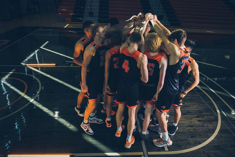 the 2022 Doane Men's Basketball team huddled together on the court, raising their hands together before a game.