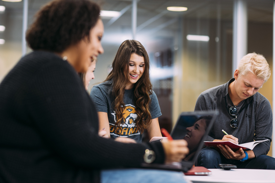 Doane studetns smiling while writing in a journal, reading from a book, and looking at their phone respectively.