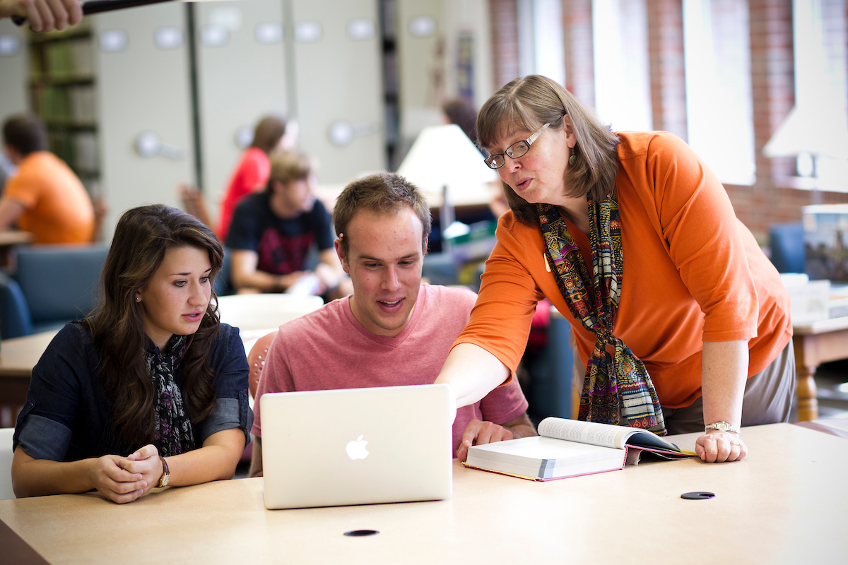 Doane teacher gesturing at a computer while two students watch