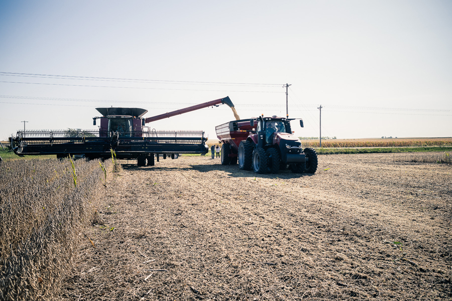 Farming combine in a field harvesting crops and depositing them in a truck bed.