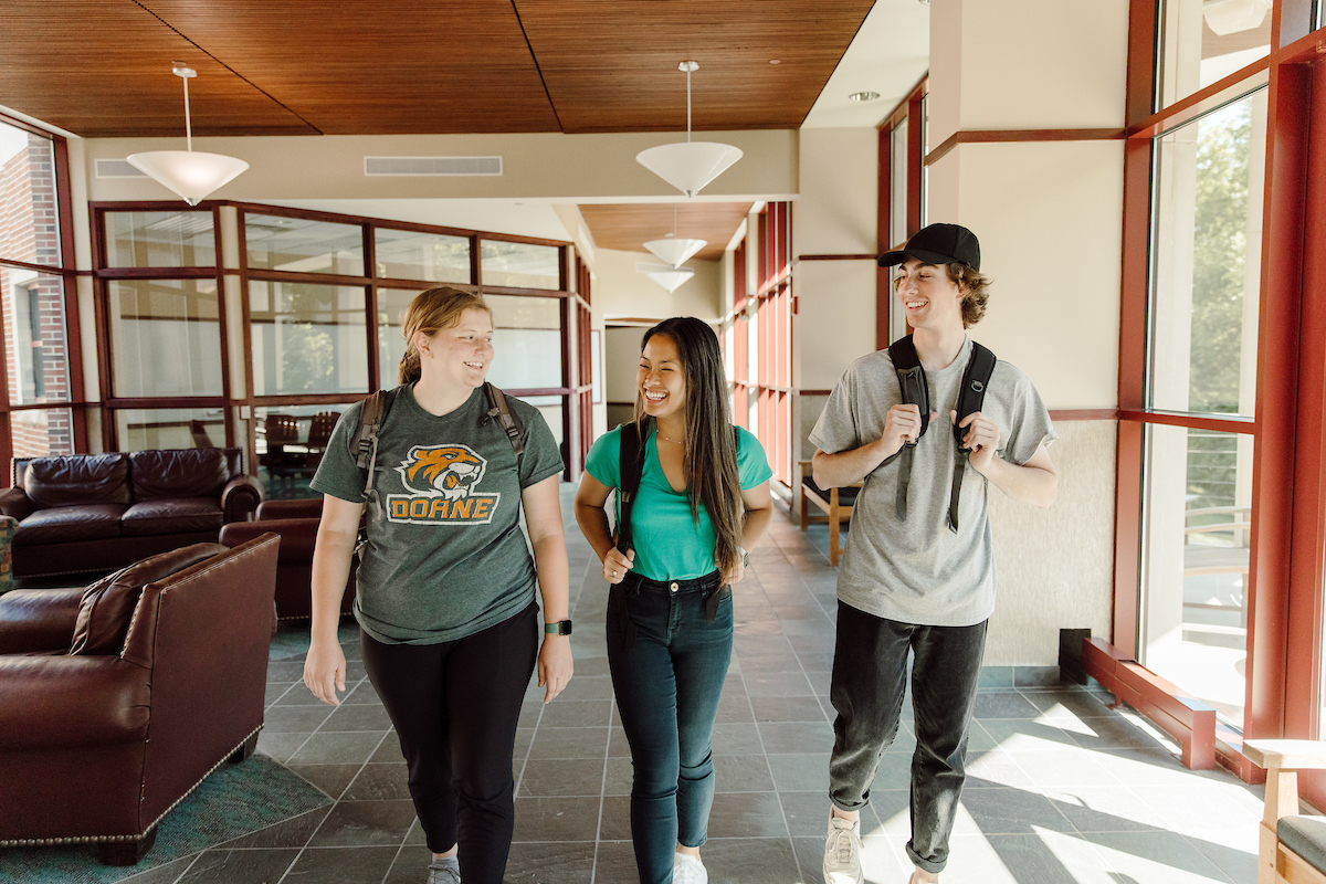 three Doane students walking through a campus building, laughing, and having a conversation.