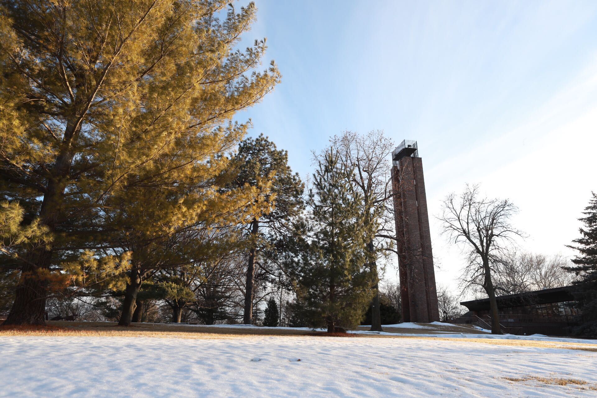 Image of Merrill Tower and surrounding trees. There is some snow on the ground, melted in some places to show brown grass peeking through. 