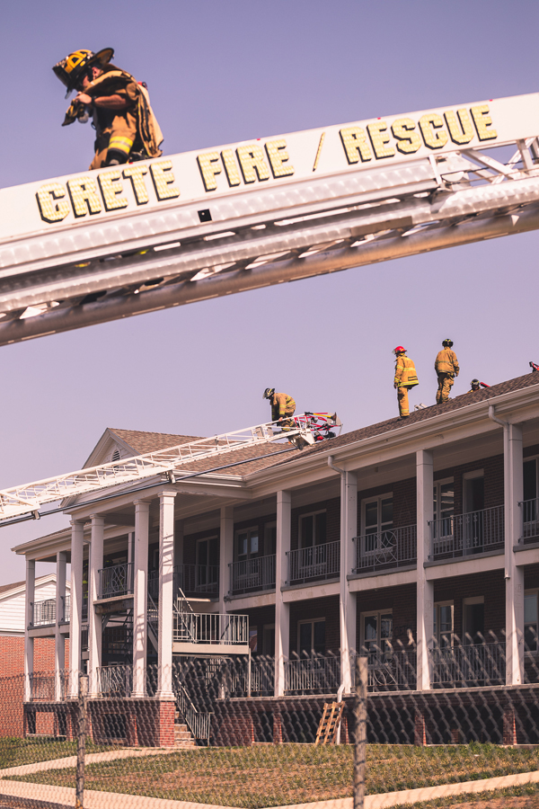 A firefighter descends from the roof of Burrage Hall on the ladder of one of Crete Volunteer Fire Department's trucks. Other firefighters practice cutting ventilation holes in the roof of the residence hall, which will be demolished later this summer. 