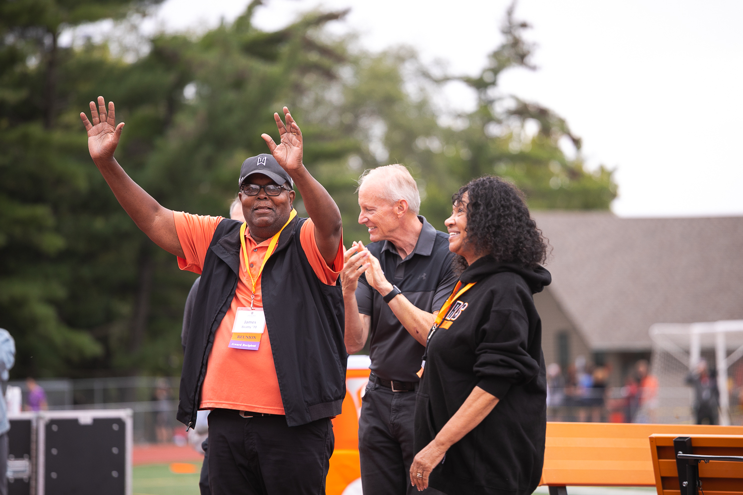 Jim Beatty holds up both arms to wave to the crowd at the 2021 Doane Homecoming football game. Behind him are Dr. Roger Hughes, Doane president, and Beatty's spouse, Earlene Beatty. 