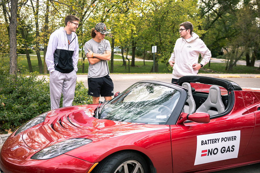 Three Doane students admire a sporty, bright red Tesla roadster.