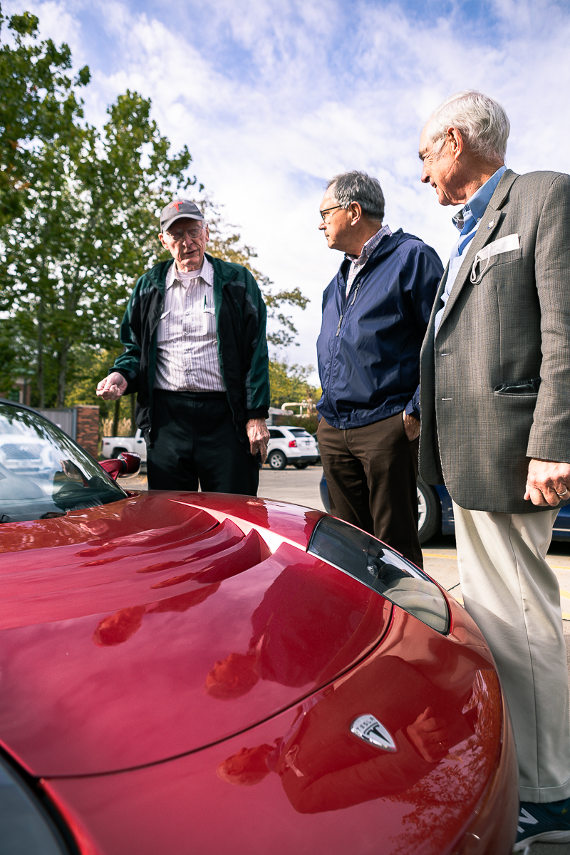 Dr. Don Cox, Dr. Russ Souchek and Ken Haar stand together next to Cox's red Tesla roadster. 