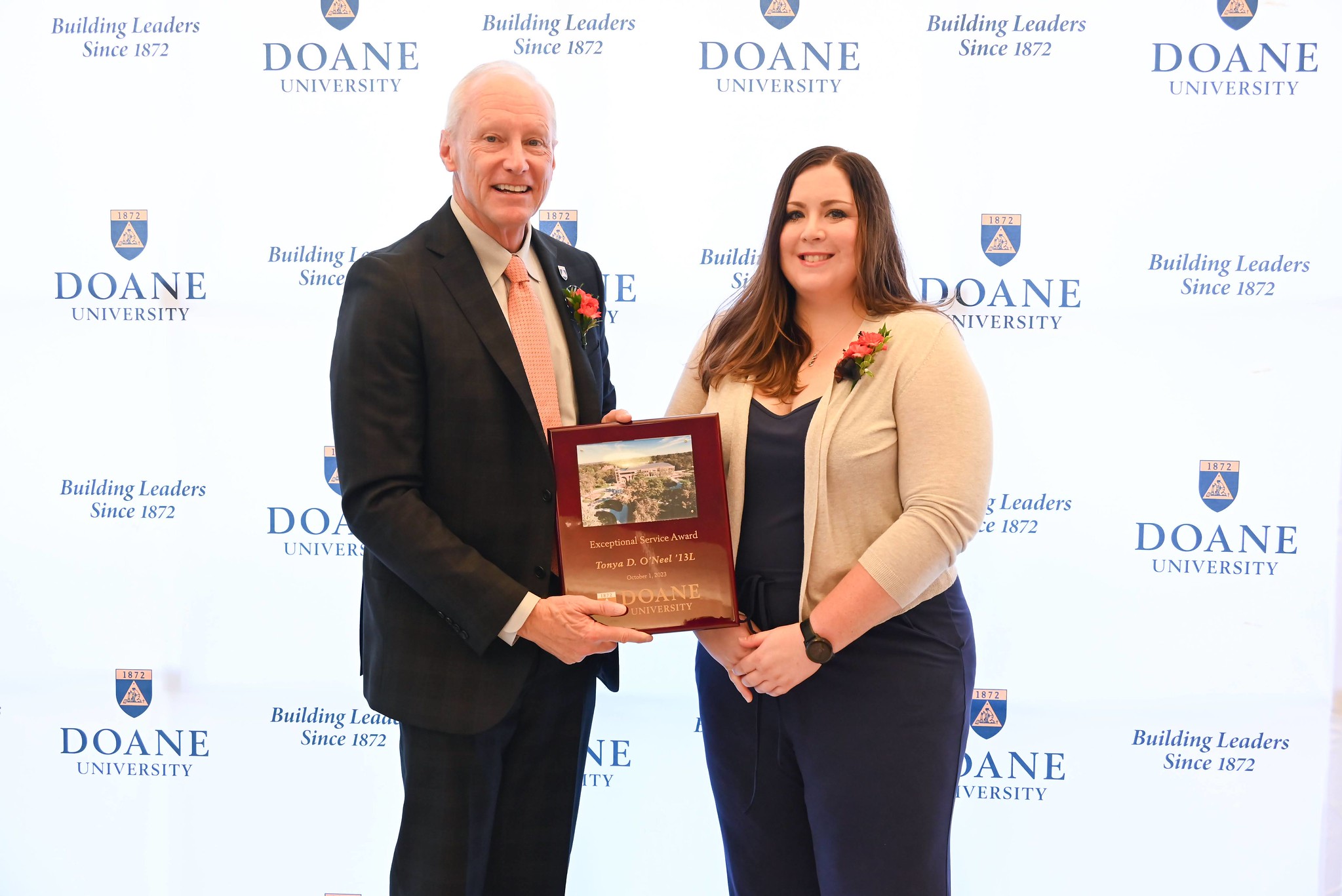 Image of Tonya O'Neel standing next to Dr. Roger Hughes in front of a white background with a pattern of Doane University's shield logo and text that reads "Building Leaders Since 1872."