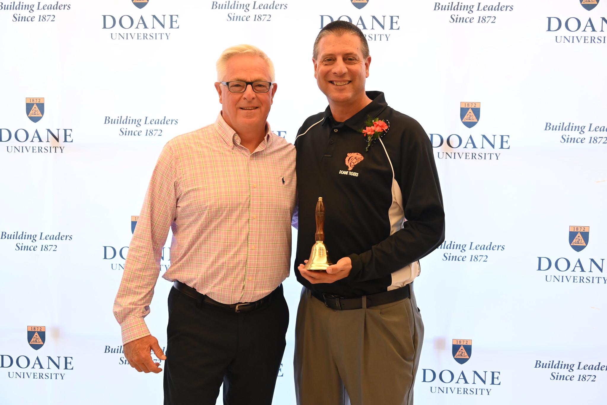 Dr. Chad Denker poses next to Ed Fye, head track and field coach at Doane University. Denker holds an old-fashioned brass bell, the award for Doane's Educator of the Year.
