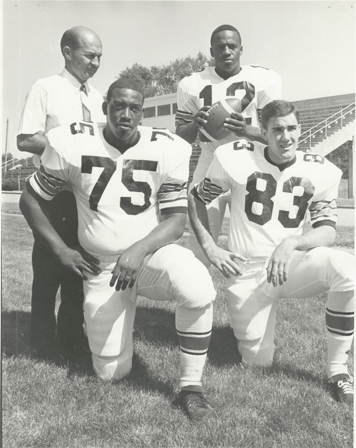 Head Football Coach Al Papik stands with three Doane football players on home turf at Simon Field. 