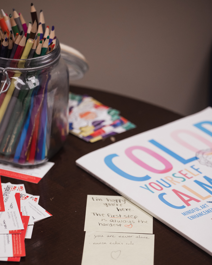 Materials sit on a table in the Counseling Center's waiting room, including a variety of colored pencils, a workbook that reads "Color Yourself Calm," business cards for Legal Aid of Nebraska and sticky notes from other students that read "I'm happy you're here," "the first step is always the hardest [heart emoji]," "you are never alone" and "nunca estás solo."