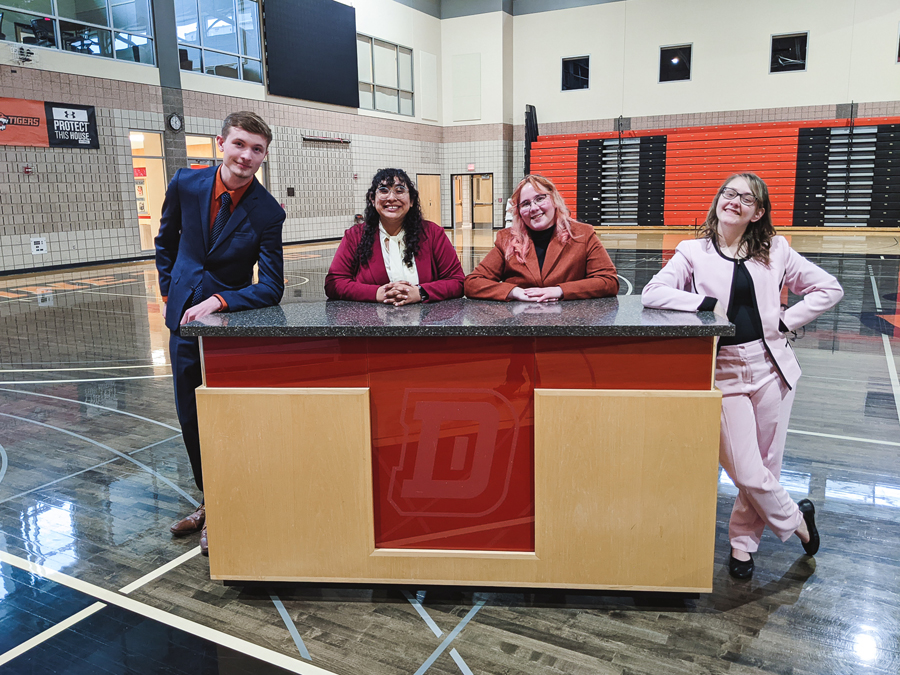Four of Doane's five forensics team members pose at a desk in their suits during a tournament held on the university's Crete campus. 