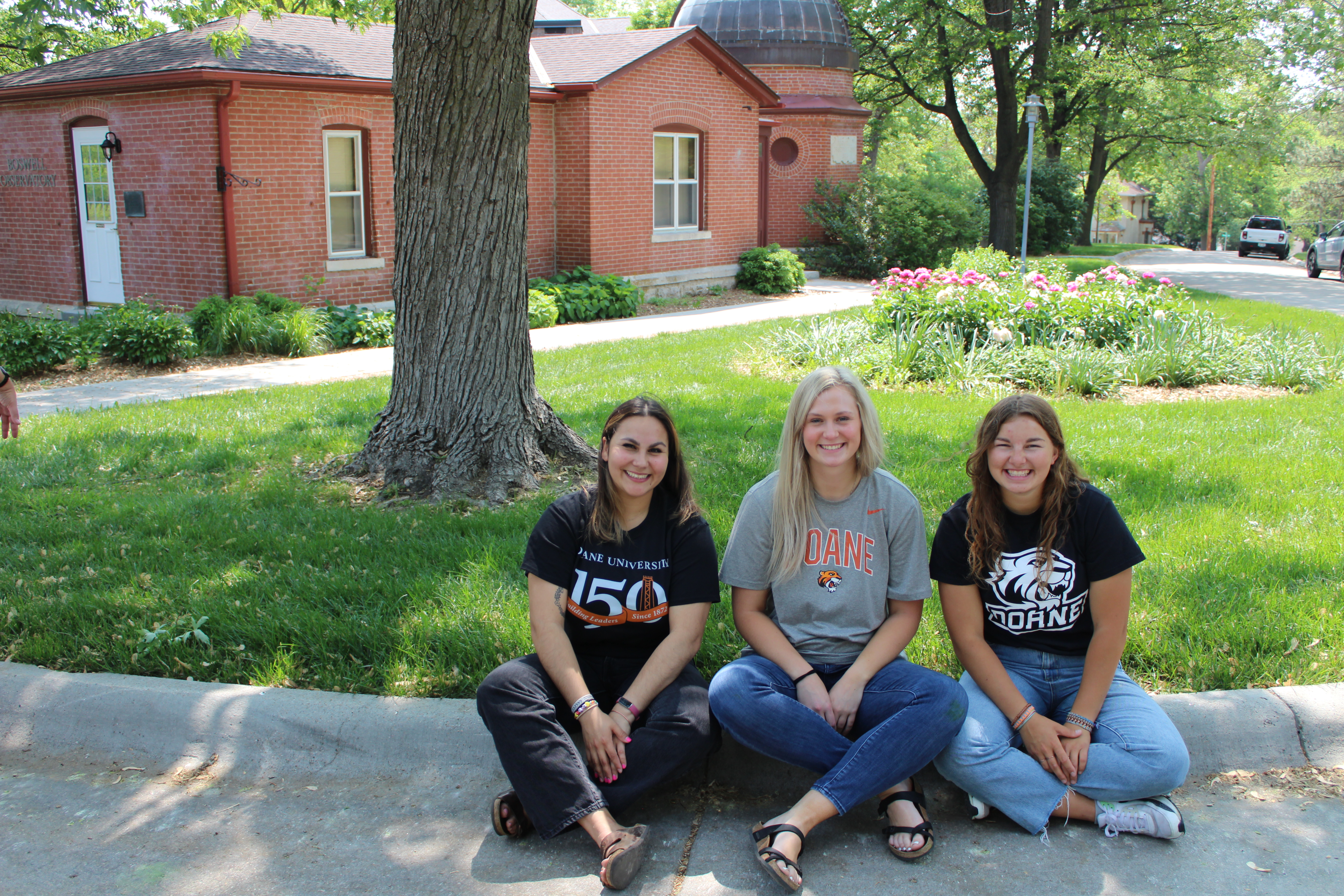 Jaiden Papik (far right) sits with fellow Tigers on Tour (TOTs), Lindsey Udell (left) and Blair Souchek (middle) on the curb in front of Boswell Observatory. 