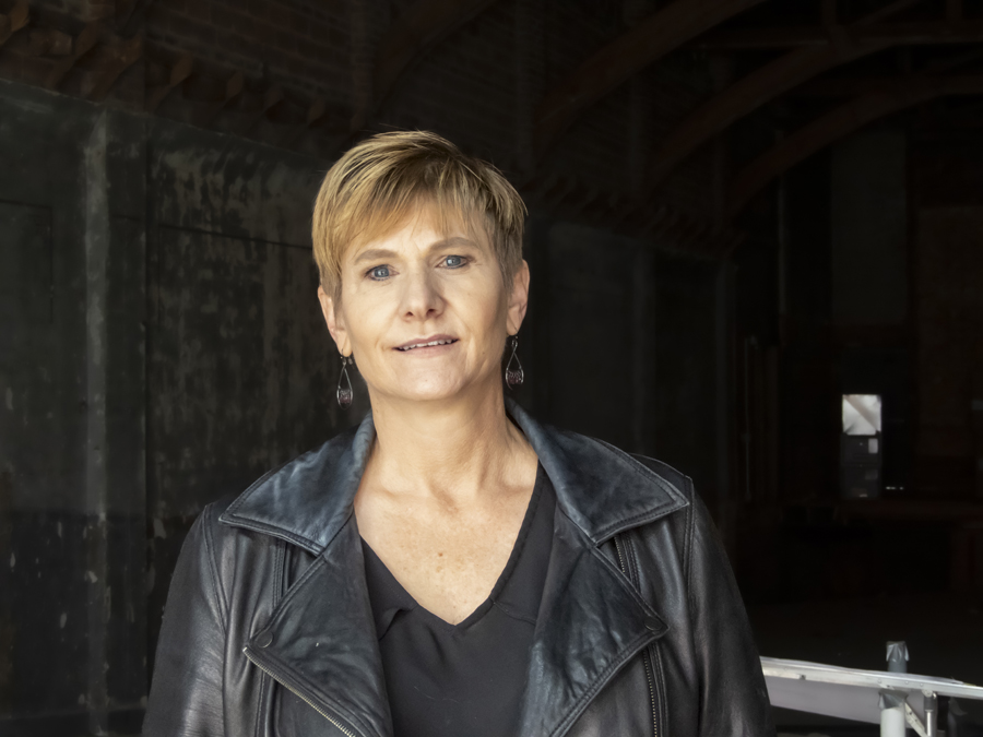 Image of Shaylene Smith ’91, inside the Isis Theatre. She wears a black v-neck shirt and a black moto jacket, with silver earrings and a pixie haircut.