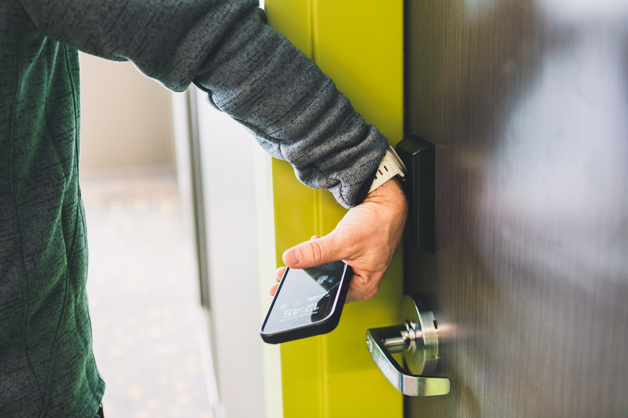 The New Hall is the first building on campus to feature electronic key entry. A man demonstrates how he uses his Apple Watch to unlock a door by placing it against a pad above the door handle.