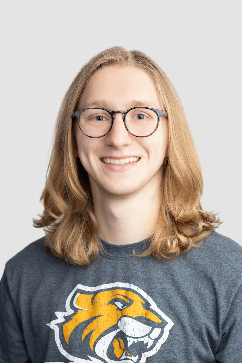 Image of a white man with shoulder-length blonde hair, blue eyes and round tortoiseshell glasses. 