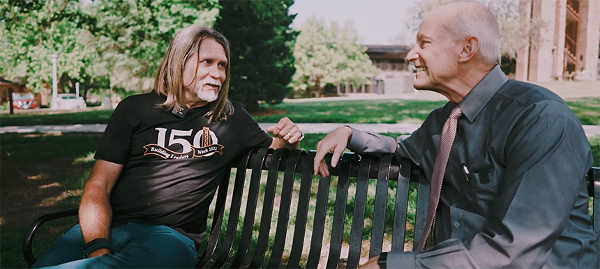Mike Hatfield, manager of grounds and facilities, sits across from President Roger Hughes on a bench in front of Merrill Tower on Doane's Crete campus.