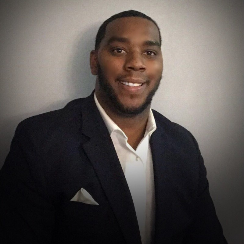 Image of Trey McGruder wearing a black blazer with a white hankerchief in his lapel and a white button-up shirt. McGruder graduated from Doane in 2015 and by September 2021, he had opened A Blessing of Hope Family Services, a private child welfare agency.