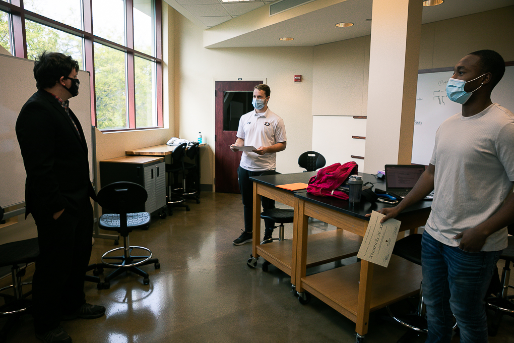 Dr. Cale Stolle presents scholarships to senior engineering students Ryan Lasauskas, left, and Kenny Kemp, right. They are standing in a classroom in the Lied Science and Mathematics building.