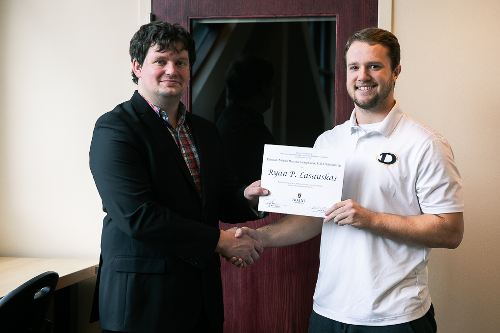 Senior engineering student Ryan Lasauskas holds up his scholarship while standing next to Dr. Cale Stolle.