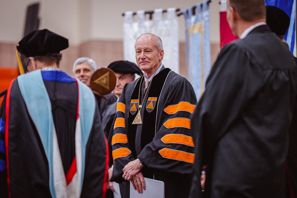 Dr. Roger Hughes stands on a stage in orange and black robes after being inaugurated as Doane University's 13th President.