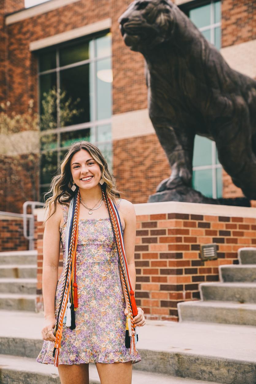 Kennedy Scheele poses with her honor cords in front of the tiger statue outside of Haddix Gymnasium. 
