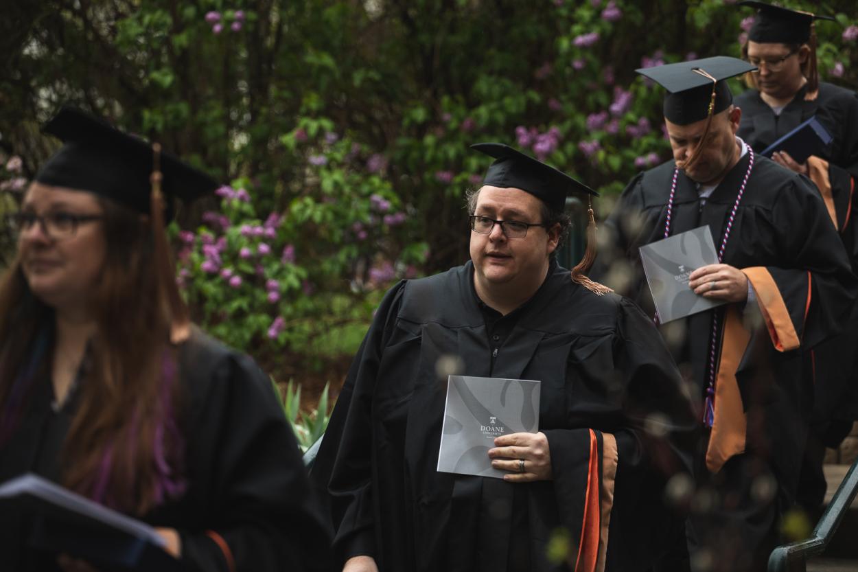 Patrick Neff '22B walks by one of Doane's Crete campus's flowering bushes during the commencement processional on May 8, 2022. 