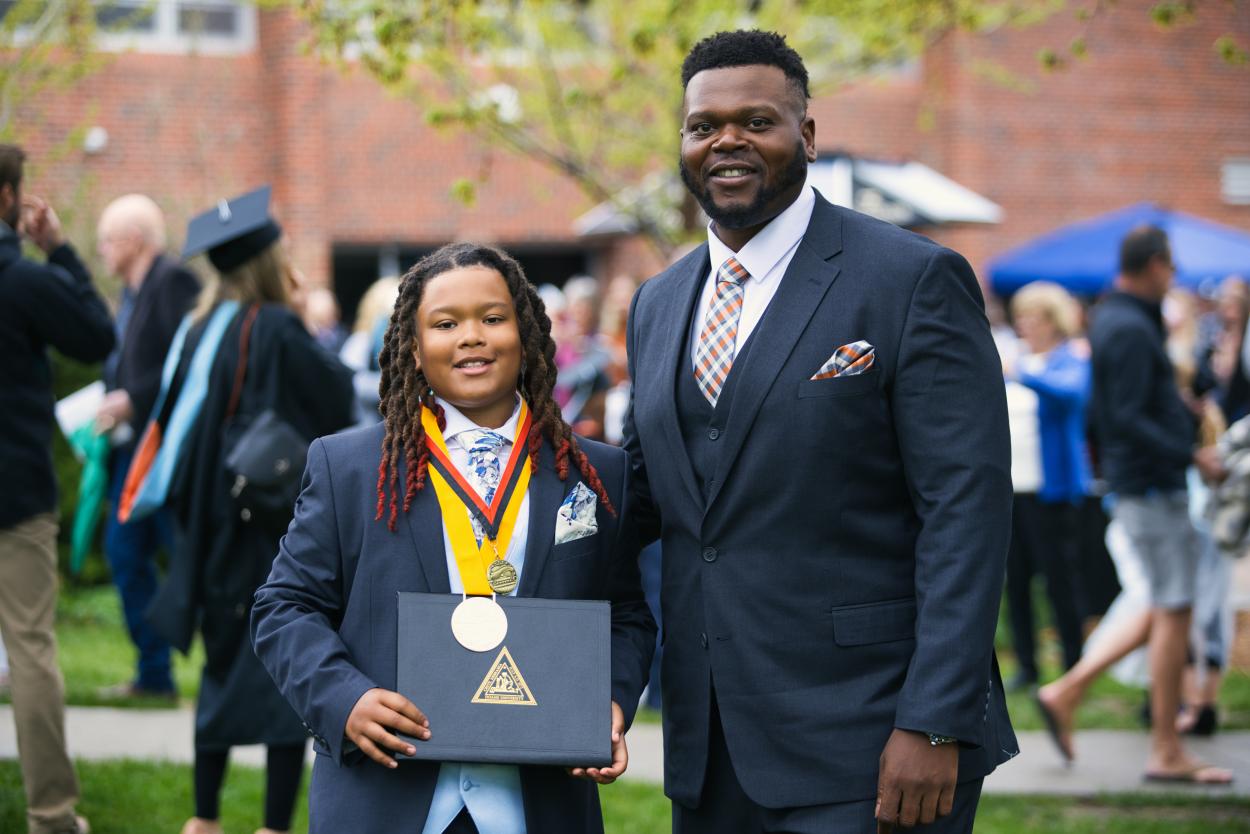 T.J. Saddler stands with his son, who's holding his degree and wearing his valedictorian hardware, at commencement on May 8, 2022.