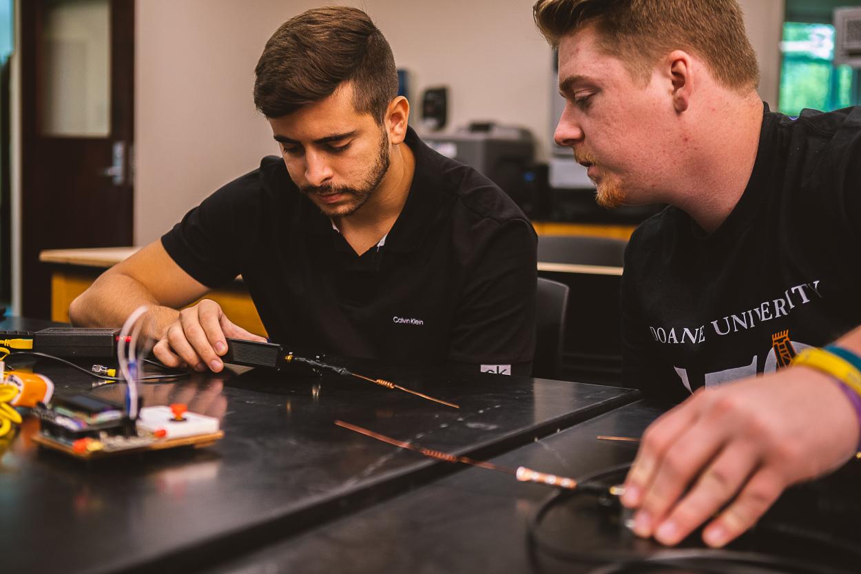 Junior Jeremey Allgeyer leans toward Henrique Henriques, senior (left), to view readings on a small black device measuring the radio signal of the transmitter he holds.
