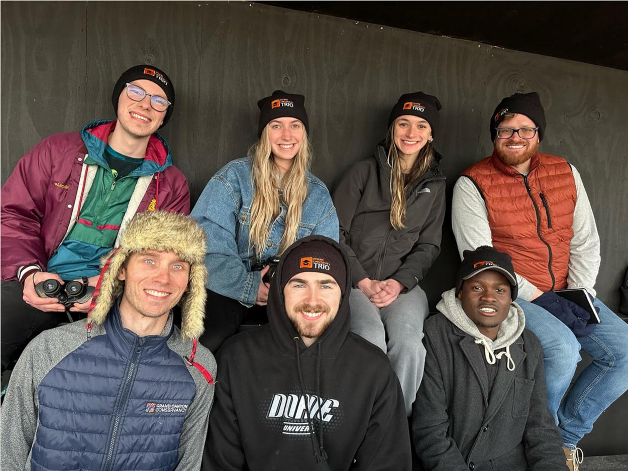 Five Doane students and staff members Jeremy Caldwell (lower left) and Blake Tobey (upper right) pose for a photo inside a crane-viewing blind at the Crane Trust Nature & Visitor's Center.