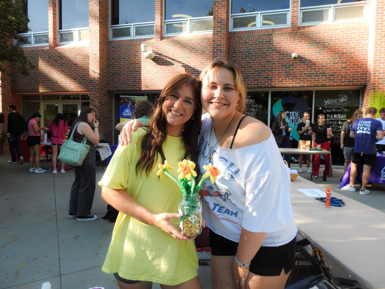 2 students posing with flowers at a booth at the Colors for Hope event