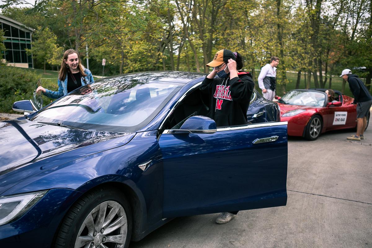 Four Doane students climb into the driver's and passenger's sides of two Tesla vehicles, a blue sedan in the foreground and a sporty red roadster in the background.