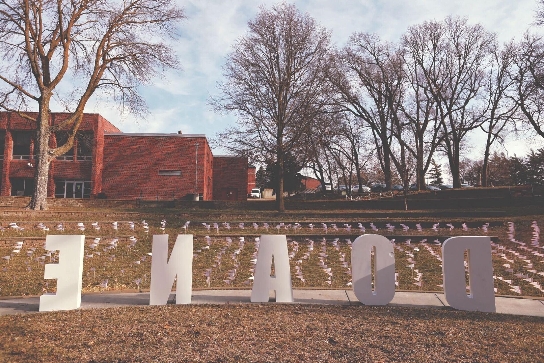 From the stage in Cassel Theatre, giant white letters spell DOANE in front of two levels of the stepped lawn filled with small orange pennants. 