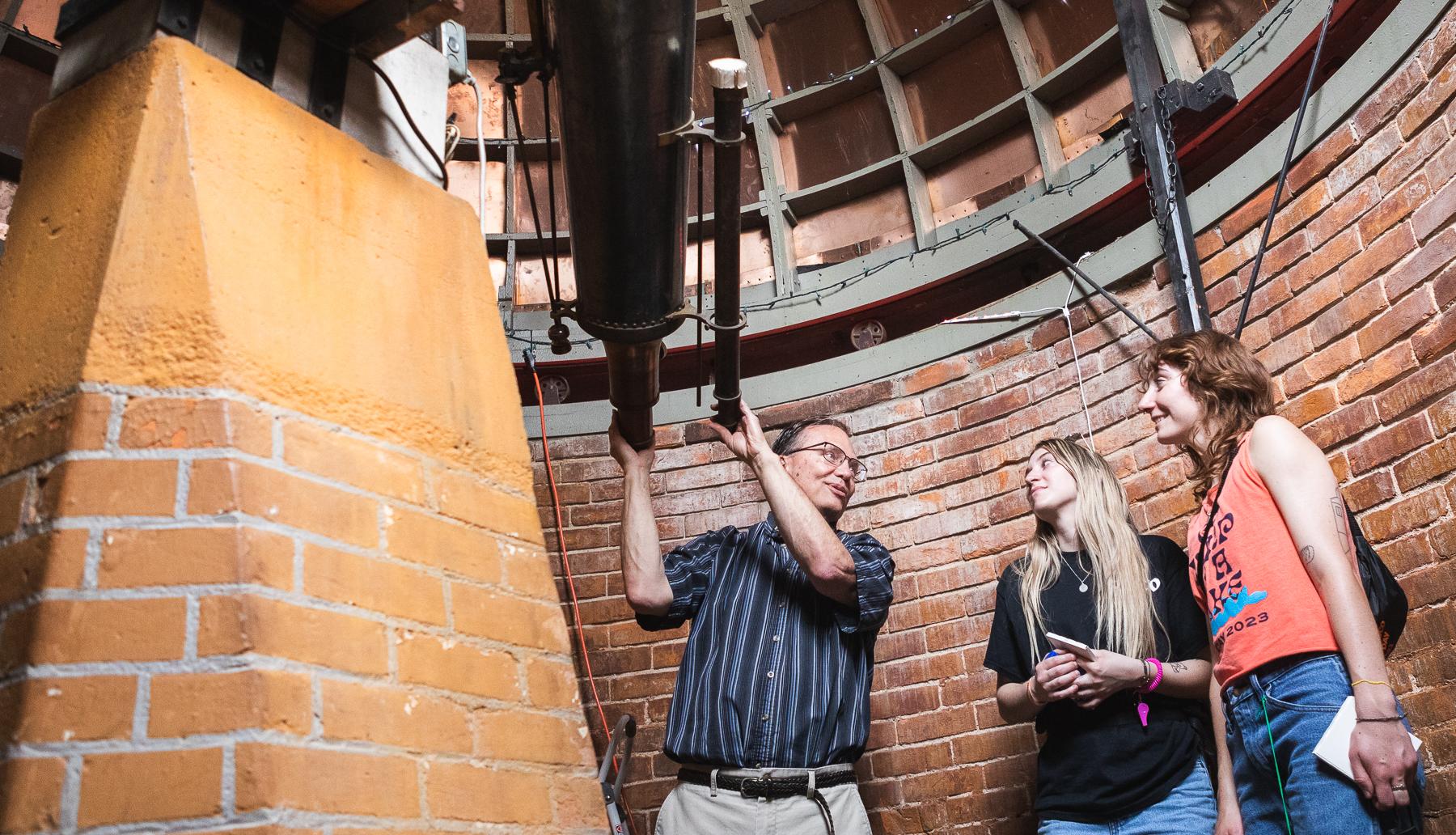 Mandi Laib (on right) and Isabel Henson speak with Dr. David Clevette in Doane's Boswell Observatory during a tour of the building on Stop Day 2023. 