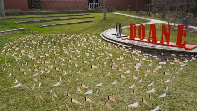Cassel Outdoor Theatre on Doane’s Crete campus has nearly 700 orange pennants on display atop the green grass. Giant letters reading G-O D-O-A-N-E can be seen near the pennants. 
